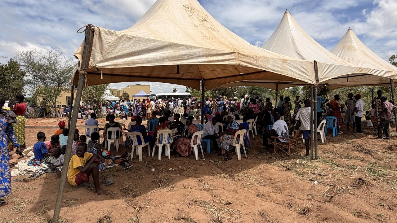 Community members seated under white tents, waiting to be seen at a community health outreach