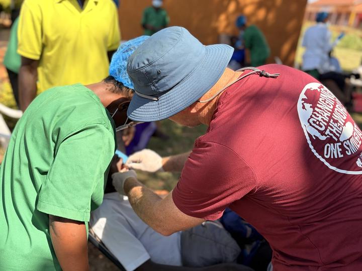 A local health worker and a visiting dentist working together on a patient outdoors